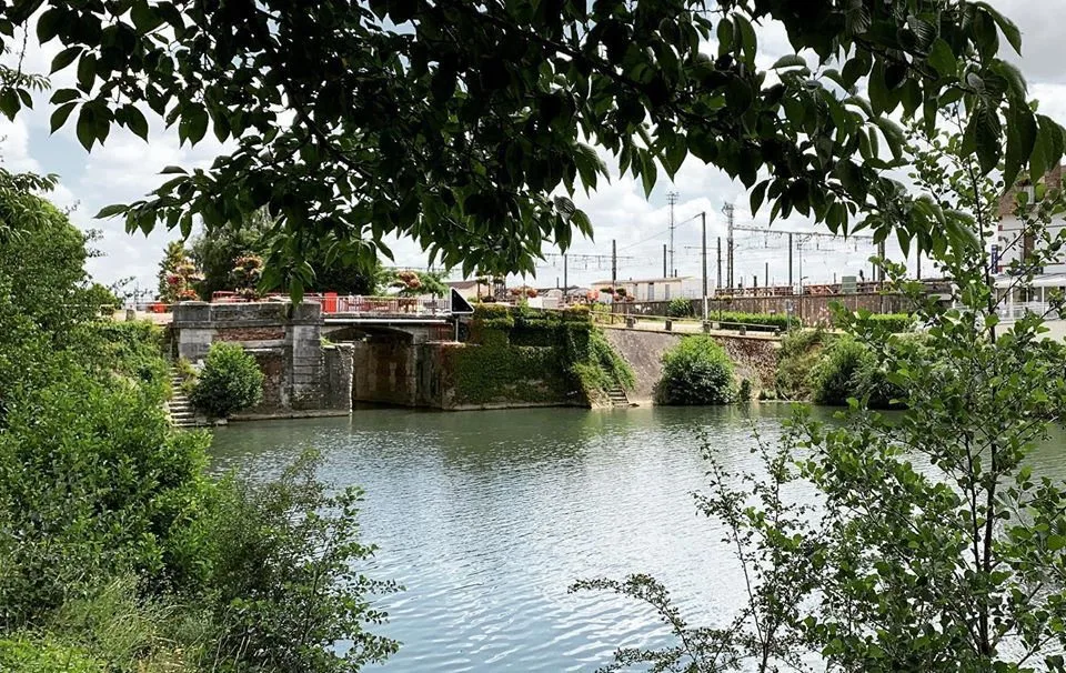 Rivière bordée d’arbres, un pont ferroviaire au loin